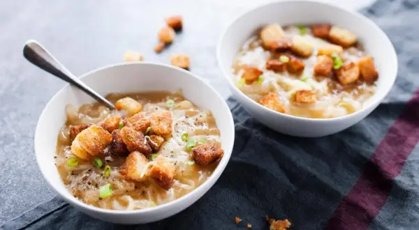Deux bols de soupe à l'oignon gratinée avec croûtons et ciboule.