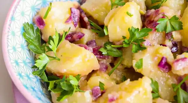 Salade de pommes de terre avec oignons rouges et persil frais dans un bol décoratif.