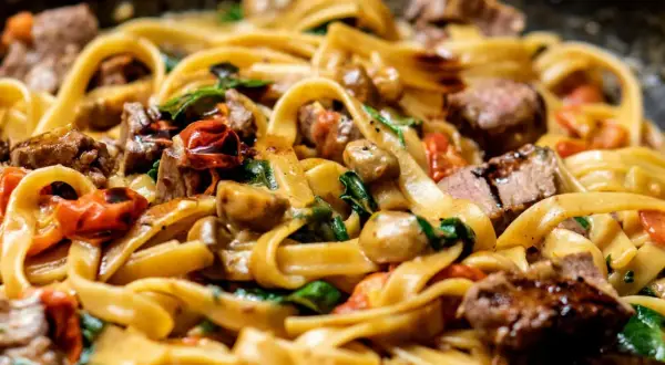Pâtes tagliatelles avec morceaux de bœuf, tomates cerises, champignons et épinards dans une sauce crémeuse.