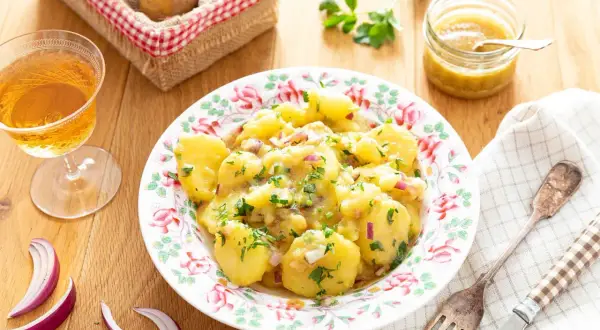 Salade de pommes de terre avec oignons rouges et persil, servie dans une assiette fleurie.