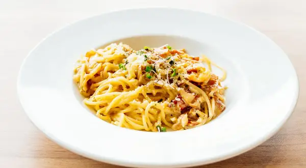 Spaghetti carbonara authentique dans une assiette blanche, garnie de lardons et de parmesan.