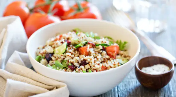 Salade de quinoa colorée avec tomates, concombre et canneberges dans un bol blanc.