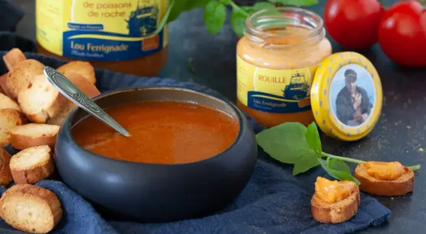 Bol de soupe de poisson, croûtons, pot de rouille et tomates.