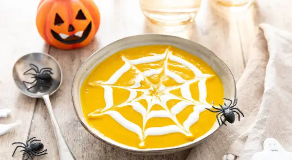 Soupe de citrouille décorée d'une toile d'araignée en crème, avec une citrouille d'Halloween et des araignées.
