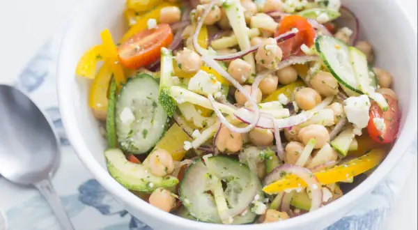 Salade de pois chiches colorée avec concombre, poivron jaune, tomate et feta dans un bol blanc.