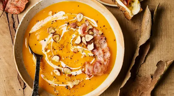 Soupe de courge butternut crémeuse garnie de lardons croustillants, noisettes et filet de crème.