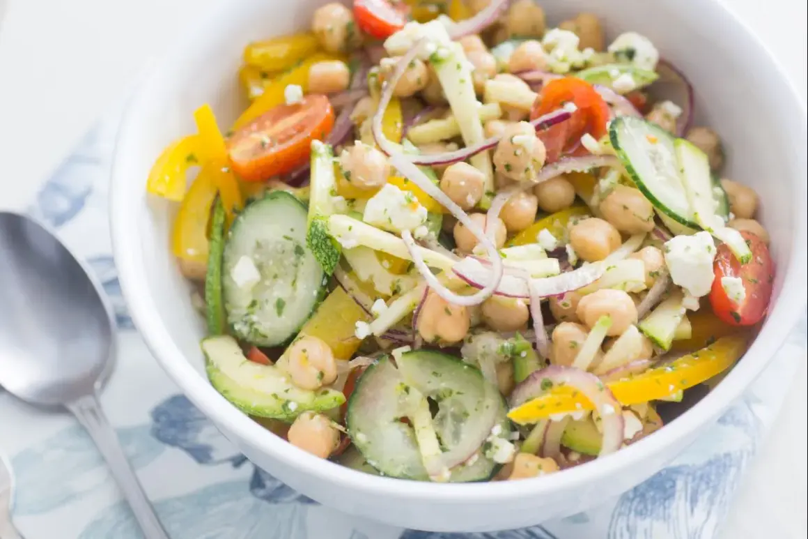 Salade de pois chiches colorée avec concombre, poivron jaune, tomate et feta dans un bol blanc.