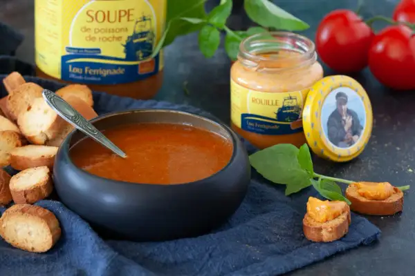 Bol de soupe de poisson, croûtons, pot de rouille et tomates.