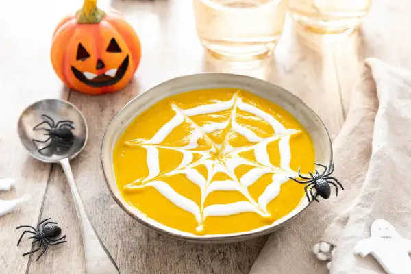 Soupe de citrouille décorée d'une toile d'araignée en crème, avec une citrouille d'Halloween et des araignées.